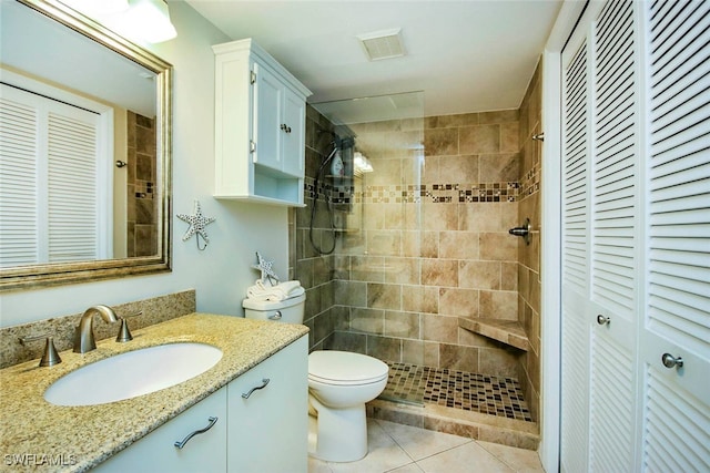 bathroom featuring tiled shower, vanity, toilet, and tile patterned flooring