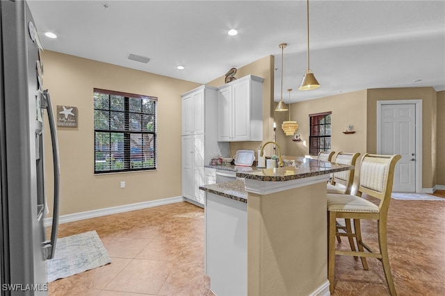 kitchen featuring white cabinets, kitchen peninsula, decorative light fixtures, a kitchen breakfast bar, and dark stone countertops