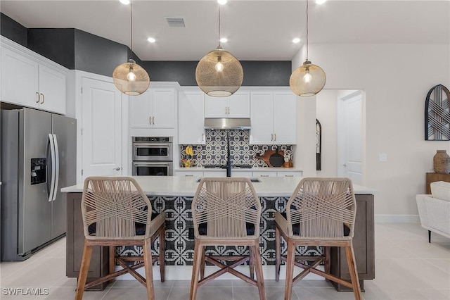 kitchen with hanging light fixtures, an island with sink, stainless steel appliances, decorative backsplash, and white cabinets