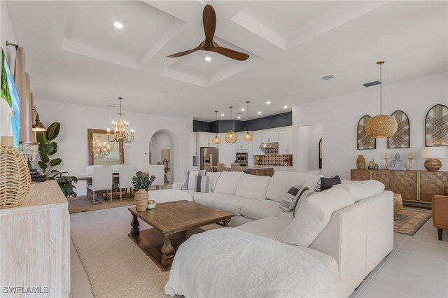 tiled living room featuring ceiling fan with notable chandelier and coffered ceiling