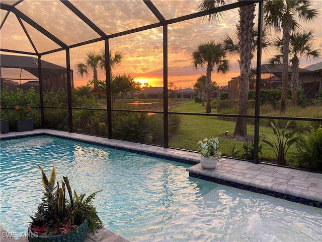 pool at dusk featuring a lanai and a lawn