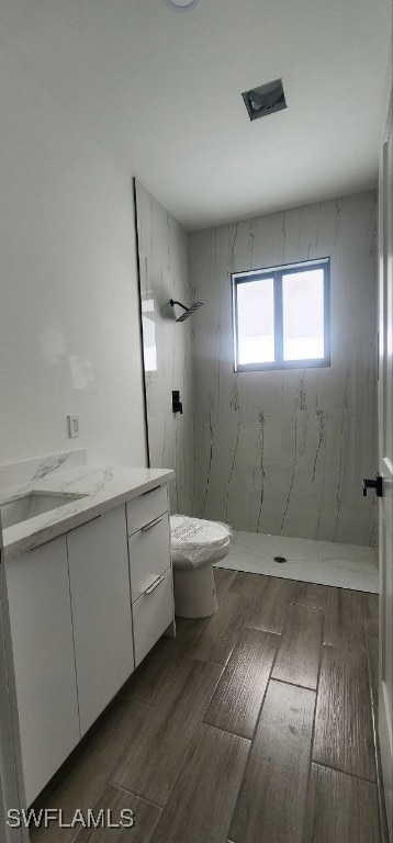 bathroom featuring tiled shower, vanity, toilet, and hardwood / wood-style flooring