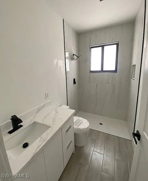 bathroom featuring a tile shower, hardwood / wood-style floors, vanity, and toilet