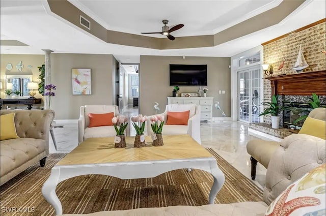 living room featuring a brick fireplace, a tray ceiling, ornamental molding, and ceiling fan