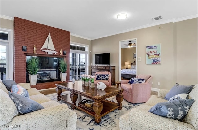 living room with a brick fireplace, ceiling fan, and crown molding