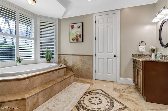 bathroom with tiled bath, vanity, and plenty of natural light