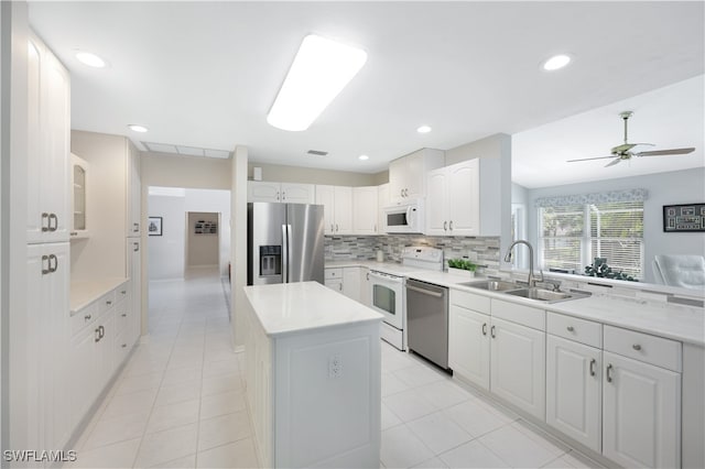 kitchen with sink, stainless steel appliances, a kitchen island, tasteful backsplash, and white cabinets