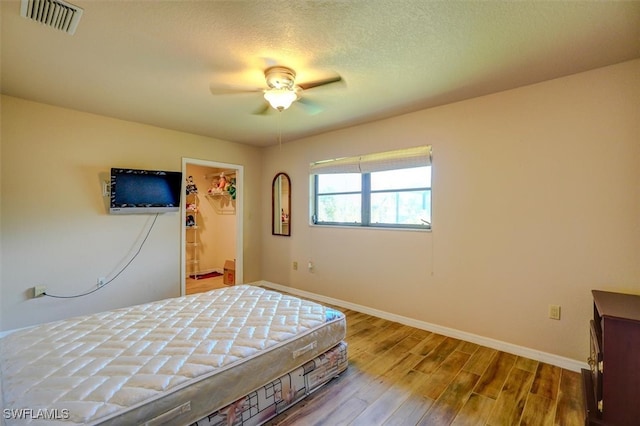 bedroom featuring a spacious closet, a closet, light wood-type flooring, a textured ceiling, and ceiling fan