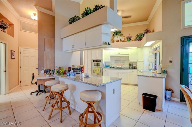 kitchen featuring light stone counters, white cabinetry, kitchen peninsula, a towering ceiling, and crown molding