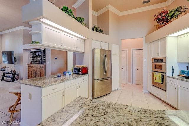 kitchen with light tile patterned flooring, light stone counters, white cabinets, stainless steel appliances, and a high ceiling