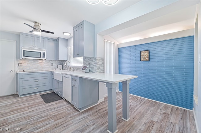 kitchen with a breakfast bar, white dishwasher, gray cabinets, light wood-type flooring, and ceiling fan