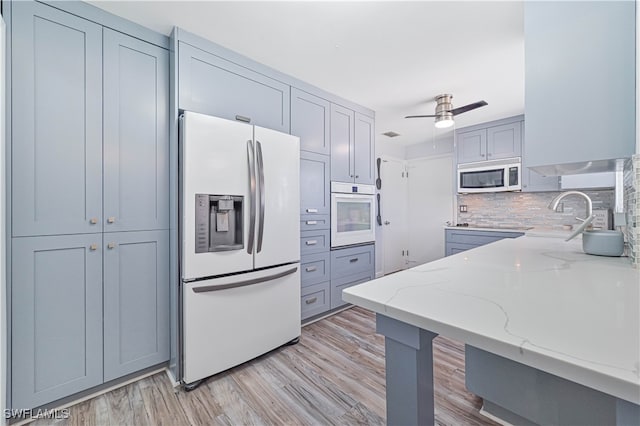 kitchen with light stone counters, light hardwood / wood-style floors, white appliances, backsplash, and ceiling fan