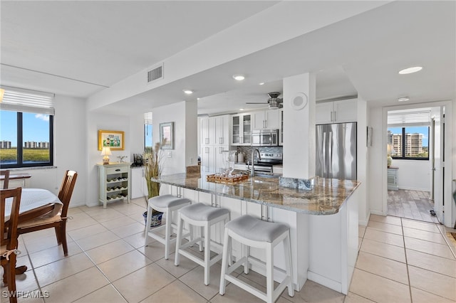 kitchen with a wealth of natural light, stainless steel appliances, kitchen peninsula, and white cabinetry