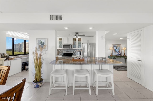 kitchen featuring dark stone counters, stainless steel appliances, white cabinets, and tasteful backsplash