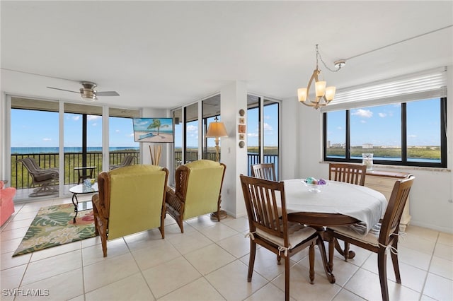 tiled dining space featuring ceiling fan with notable chandelier and a water view