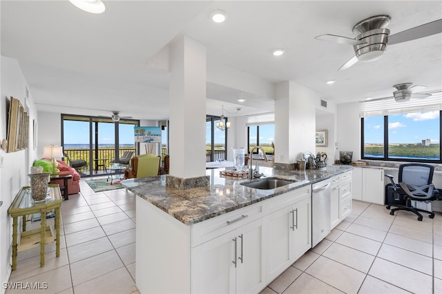 kitchen with dark stone counters, dishwasher, a kitchen island with sink, sink, and white cabinetry