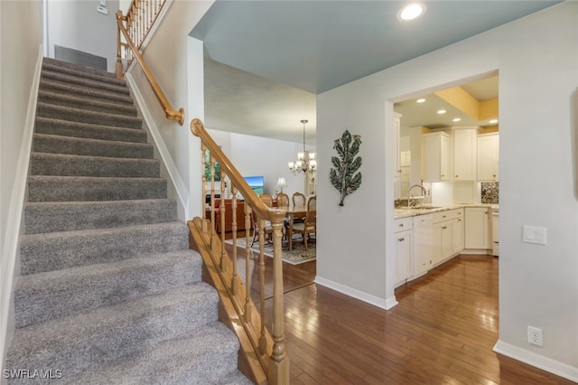 staircase featuring a notable chandelier, sink, and wood-type flooring