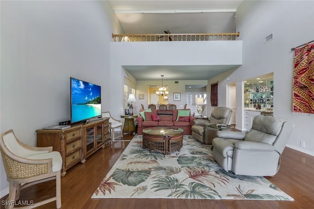 living room featuring a high ceiling, bar, dark wood-type flooring, and an inviting chandelier