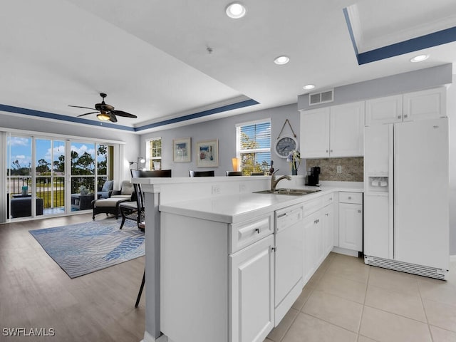 kitchen with a raised ceiling, kitchen peninsula, white appliances, and white cabinetry