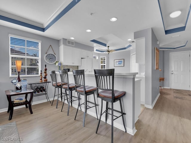 kitchen with a raised ceiling, kitchen peninsula, white cabinetry, and a breakfast bar