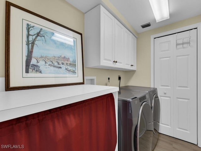 clothes washing area with cabinets, light hardwood / wood-style flooring, and washing machine and clothes dryer