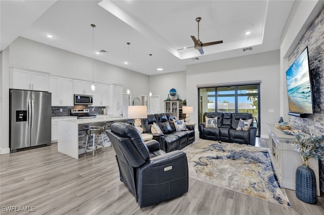 living room with light hardwood / wood-style floors, a tray ceiling, and ceiling fan