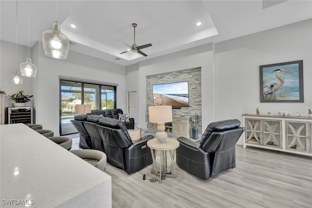 living room featuring a tray ceiling, light wood-type flooring, and ceiling fan