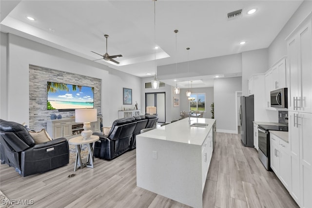 kitchen featuring light wood-type flooring, white cabinetry, stainless steel appliances, pendant lighting, and a kitchen island with sink