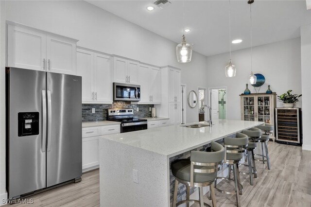 kitchen featuring white cabinetry, stainless steel appliances, beverage cooler, and an island with sink