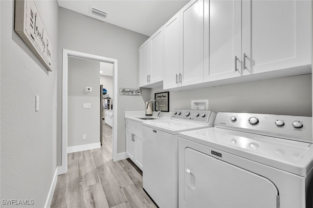 laundry area featuring sink, washing machine and clothes dryer, light hardwood / wood-style floors, and cabinets