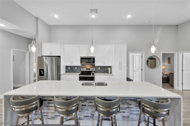 kitchen featuring a large island with sink, appliances with stainless steel finishes, a breakfast bar area, and hanging light fixtures