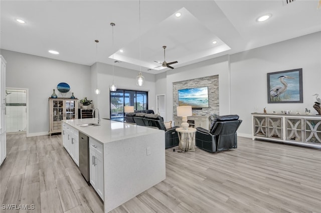 kitchen with hanging light fixtures, a center island with sink, white cabinetry, light wood-type flooring, and sink