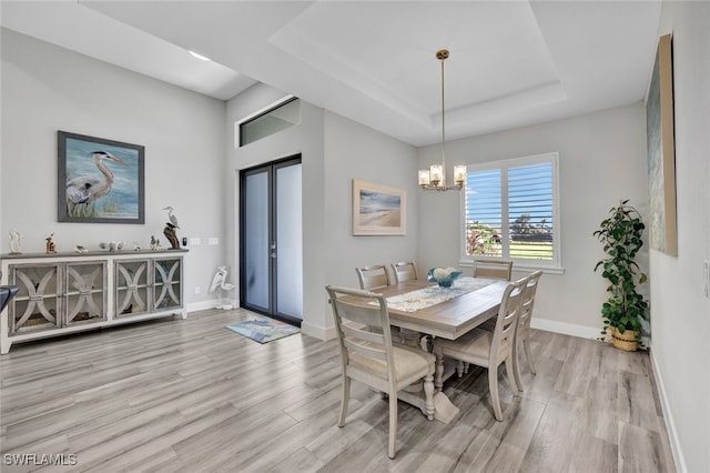 dining room featuring a chandelier, french doors, light hardwood / wood-style floors, and a raised ceiling