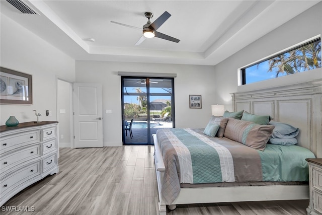 bedroom featuring access to exterior, a tray ceiling, light wood-type flooring, and ceiling fan