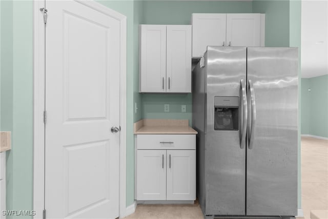 kitchen featuring stainless steel refrigerator with ice dispenser, light tile patterned floors, and white cabinetry