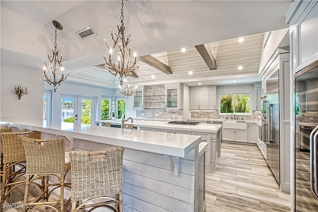 kitchen with hanging light fixtures, a large island with sink, backsplash, and a healthy amount of sunlight