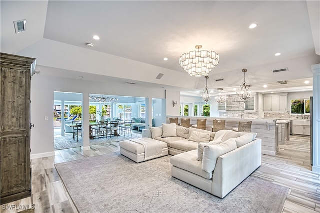 living room featuring an inviting chandelier, light hardwood / wood-style floors, and a raised ceiling