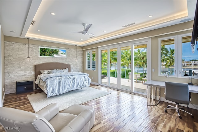 bedroom featuring ceiling fan, a raised ceiling, hardwood / wood-style floors, and access to exterior