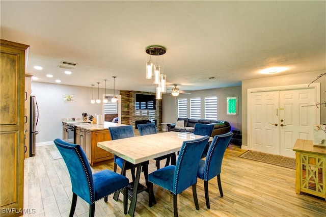 dining area with light wood-type flooring, a stone fireplace, and ceiling fan