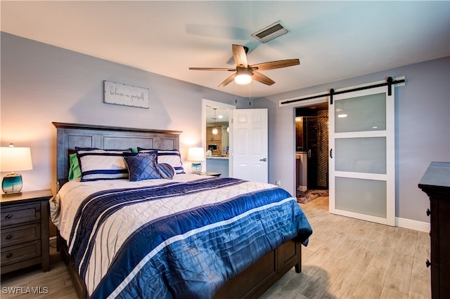 bedroom with ceiling fan, light wood-type flooring, and a barn door