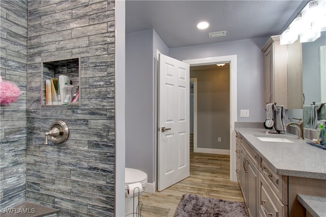 bathroom with vanity, hardwood / wood-style floors, toilet, and tiled shower