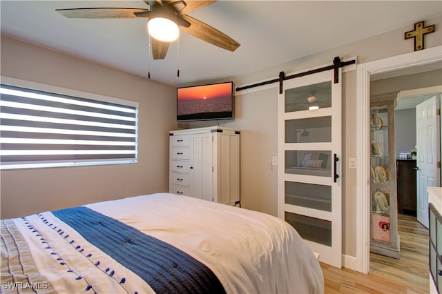 bedroom with ceiling fan, light wood-type flooring, and a barn door