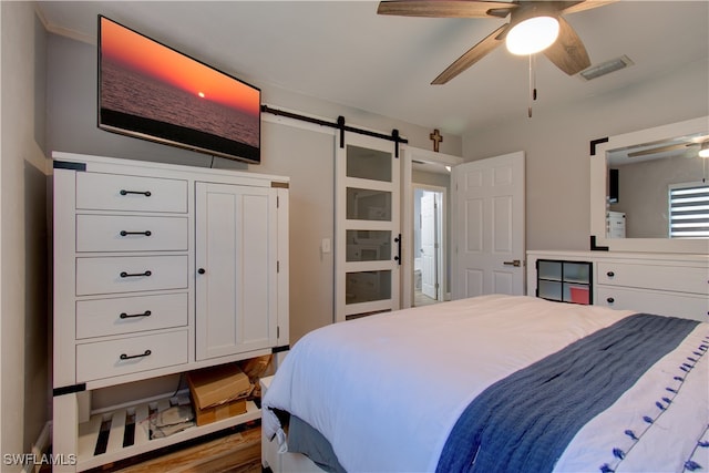 bedroom with a barn door, wood-type flooring, and ceiling fan