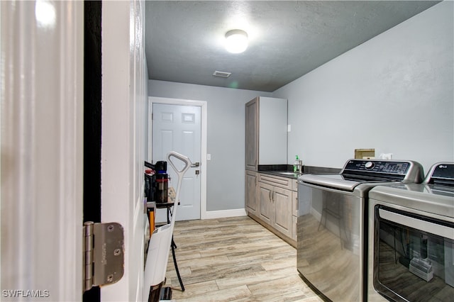 washroom featuring cabinets, light wood-type flooring, independent washer and dryer, and a textured ceiling