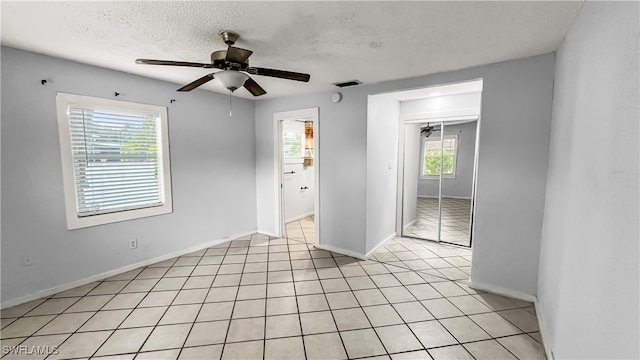 spare room with ceiling fan, a textured ceiling, light tile patterned flooring, and a wealth of natural light