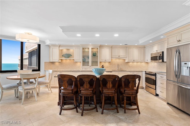 kitchen featuring cream cabinets, a kitchen island, ornamental molding, stainless steel appliances, and a water view