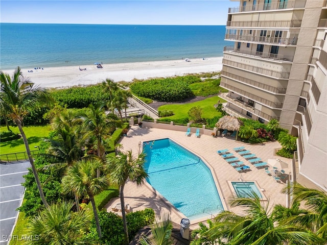 view of swimming pool featuring a water view, a patio, and a beach view