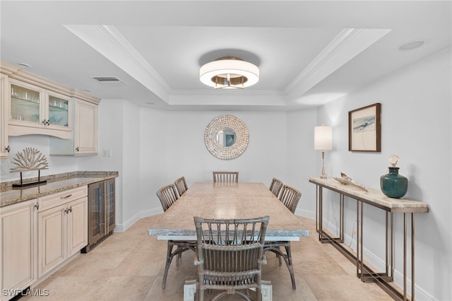 dining area with ornamental molding, beverage cooler, and a raised ceiling