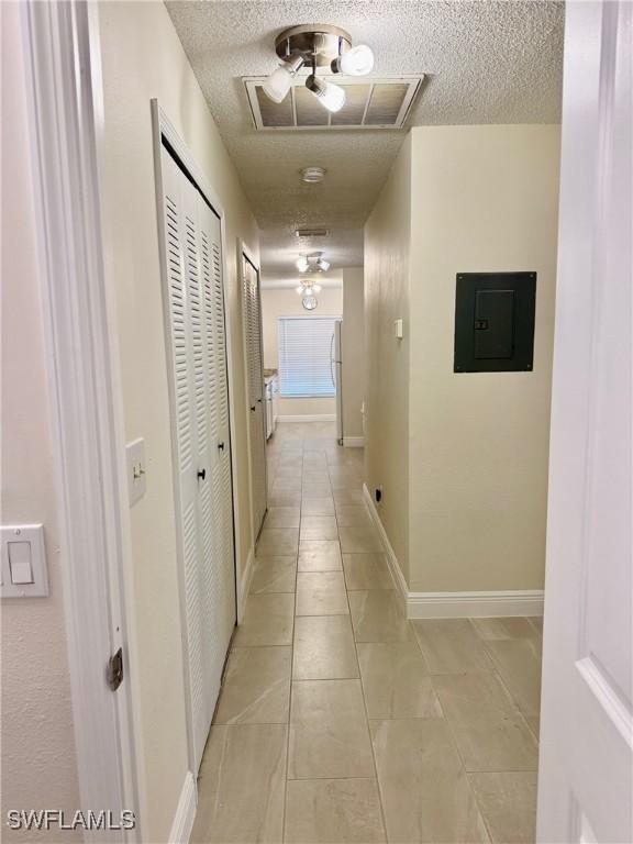 hall with electric panel, light tile patterned floors, and a textured ceiling