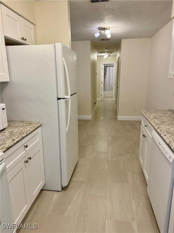 kitchen featuring white cabinets, a textured ceiling, white appliances, and light stone countertops